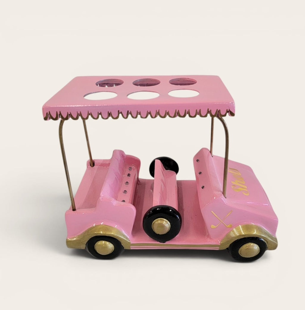 A pink wooden toy golf cart with a matching canopy, gold-colored trim, and black wheels, photographed against a plain light beige background.