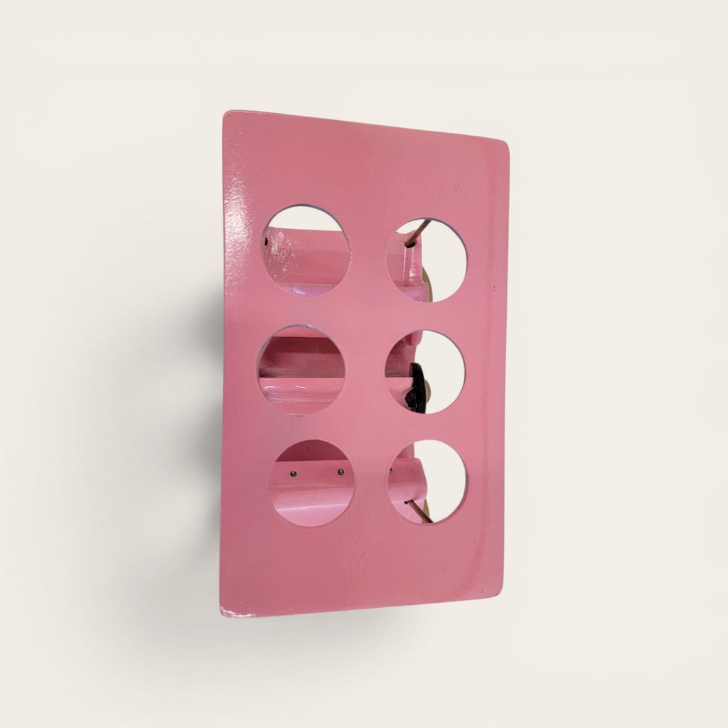 A pink rectangular wall-mounted sculpture or decorative panel with six circular cutouts, shown against a plain off-white background.