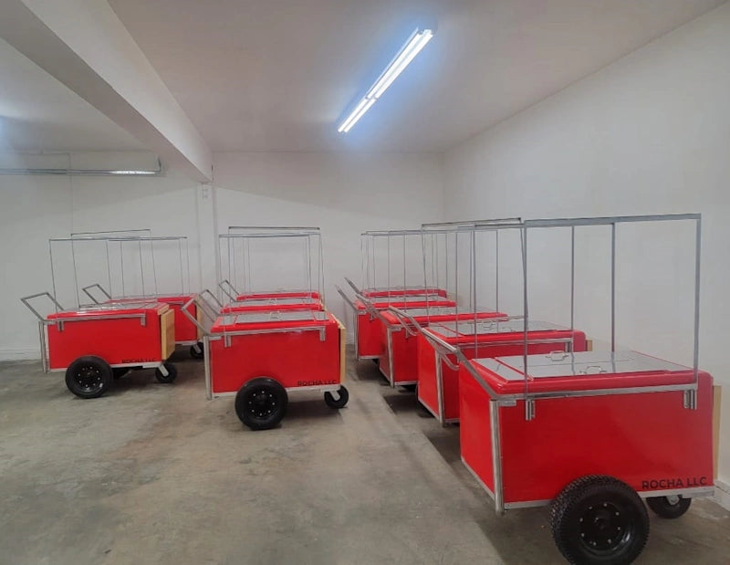 Several red food carts with silver metal frames and black wheels parked in a warehouse-like indoor space with concrete floors and white walls.