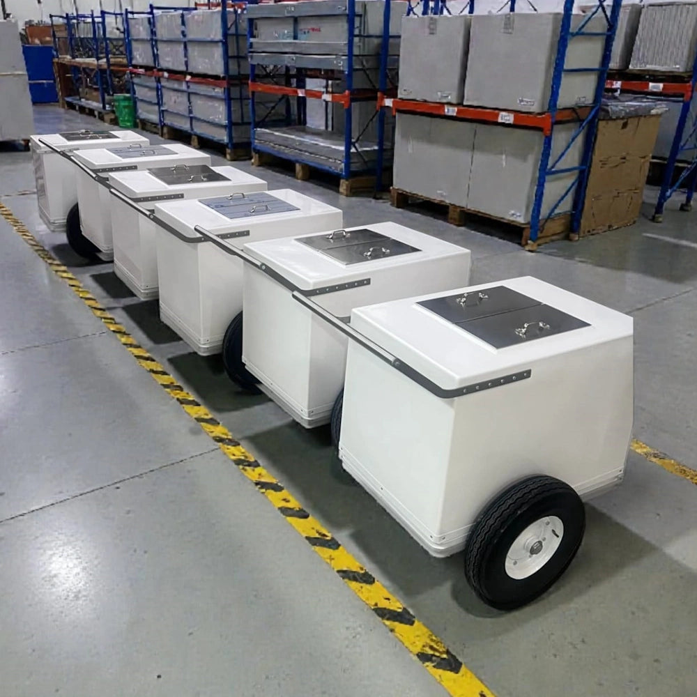 A row of white wheeled utility carts with black wheels and dark top panels, displayed in a warehouse setting with shelving and other equipment in the background.